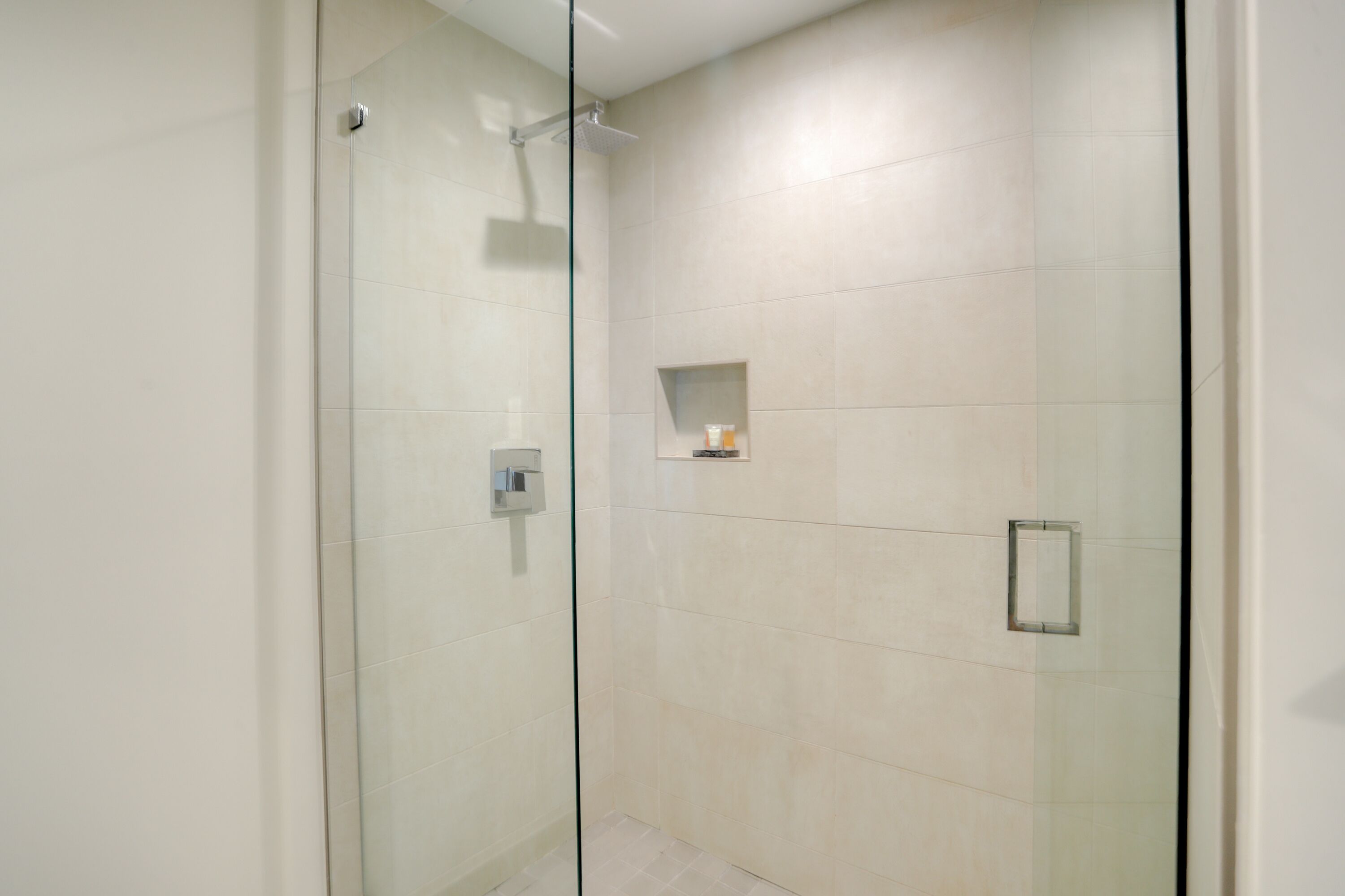 A modern bathroom with a glass-enclosed shower, tiled walls, and a small shelf with toiletries.