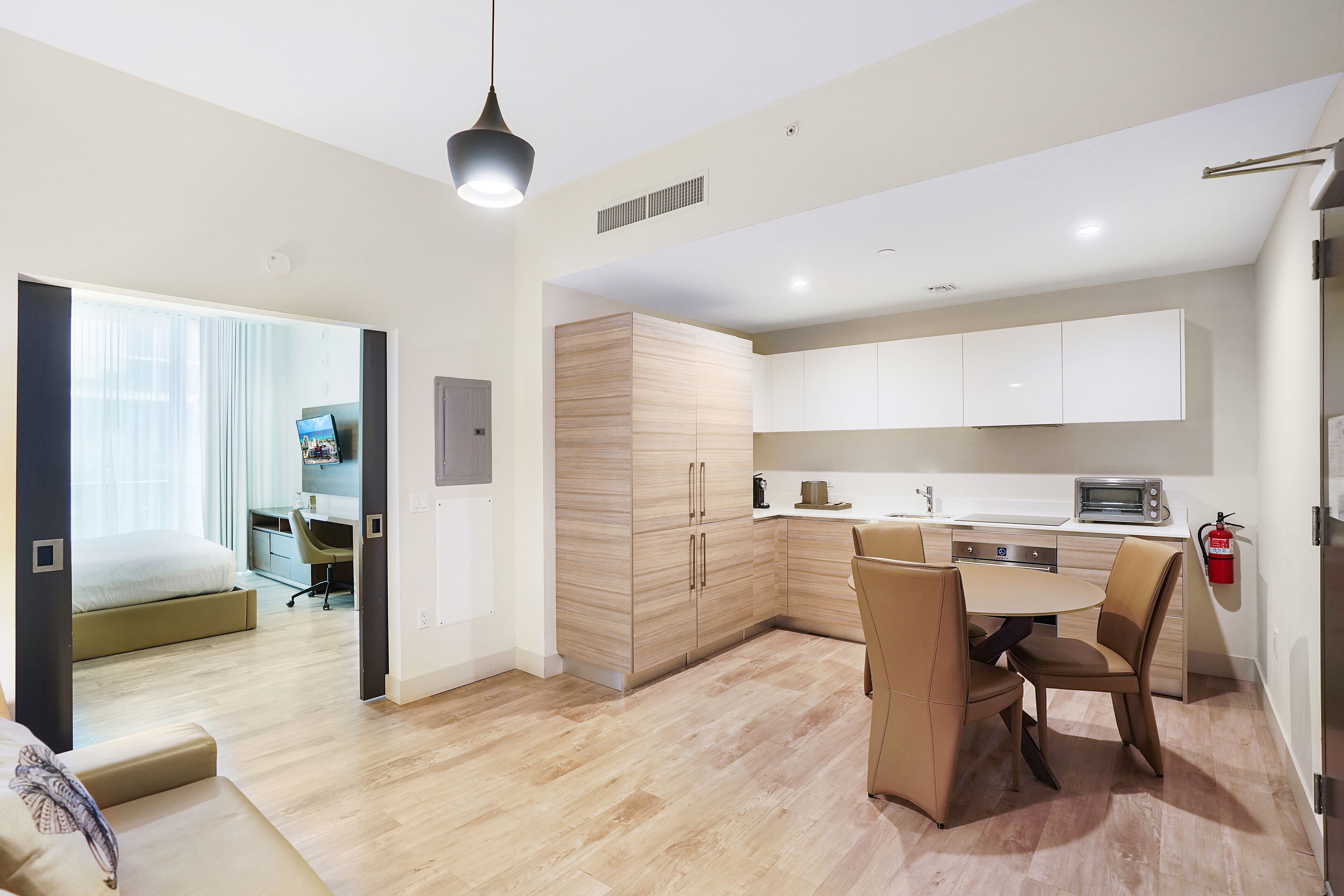 A modern apartment with a dining area, kitchenette, and a bedroom with a large window.