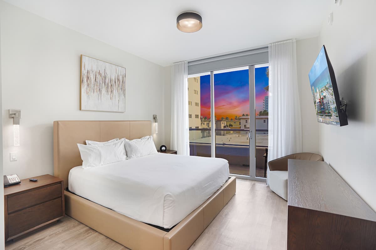 Une chambre d’hôtel moderne dotée d’un grand lit, d’un bureau, d’une télévision et offrant une vue sur le paysage urbain par la fenêtre.