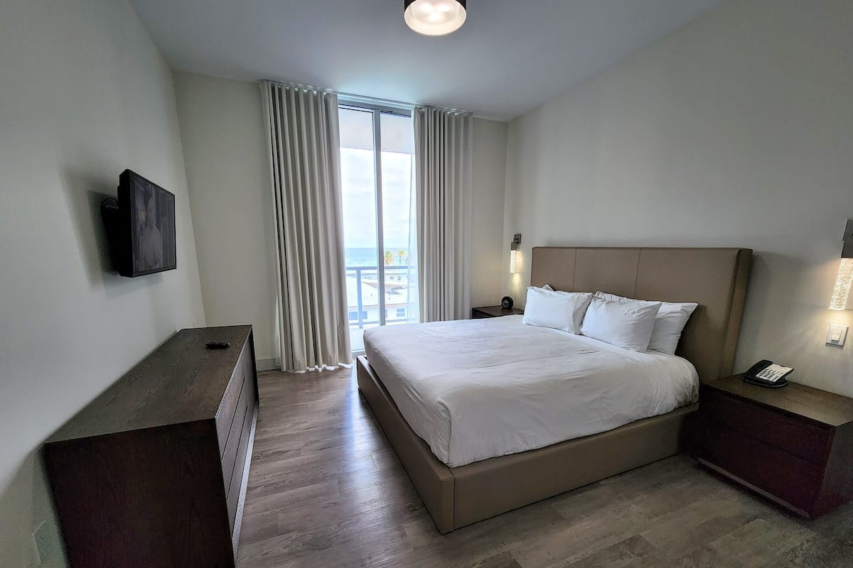 Une chambre d’hôtel avec un grand lit, un téléviseur fixé au mur, une table de chevet avec un téléphone et une vue sur l’extérieur par la fenêtre.