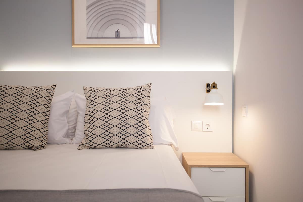 A neatly made bed with patterned pillows, a bedside table with a lamp, and a framed picture on the wall.