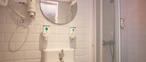 Un baño con un lavabo blanco, un espejo redondo, un secador de pelo y una ducha.