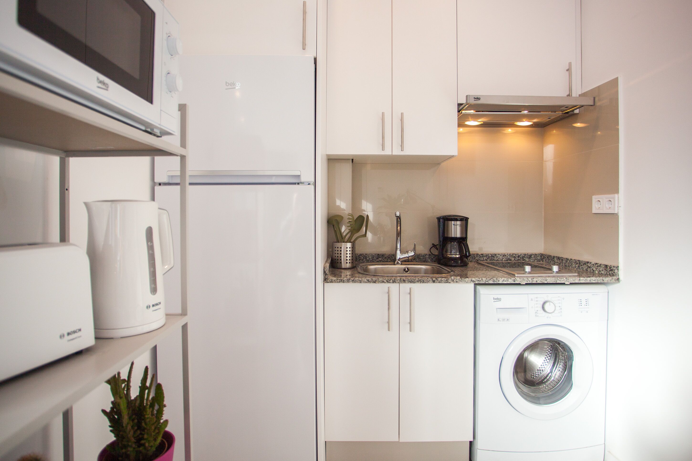 Una cocina compacta equipada con microondas, refrigerador, cafetera, lavamanos y lavadora.