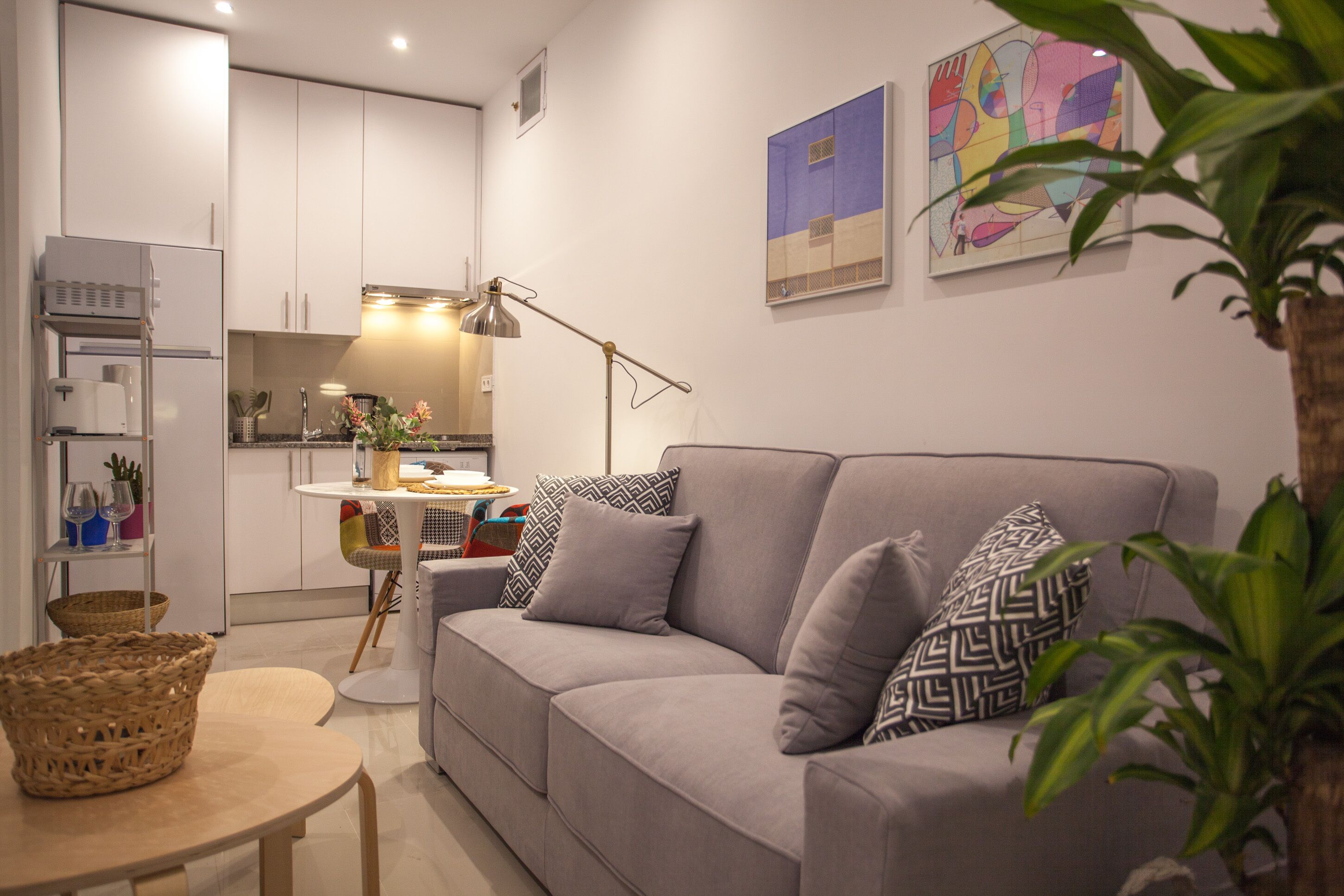 A modern living room with a grey sofa, a small round table, and a kitchen in the background.