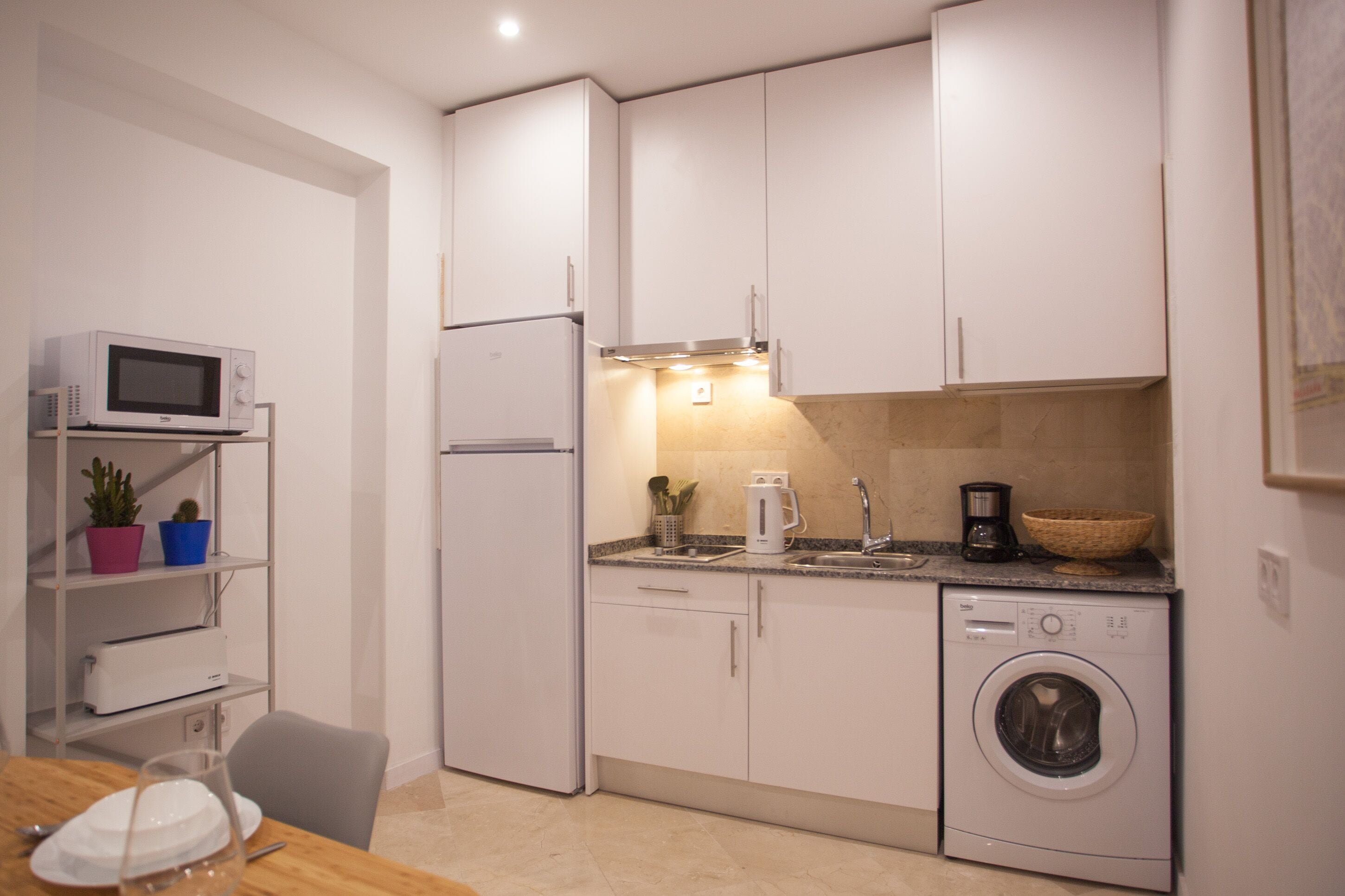 A compact kitchen with white cabinets, a microwave, a refrigerator, a coffee maker, and a washing machine.