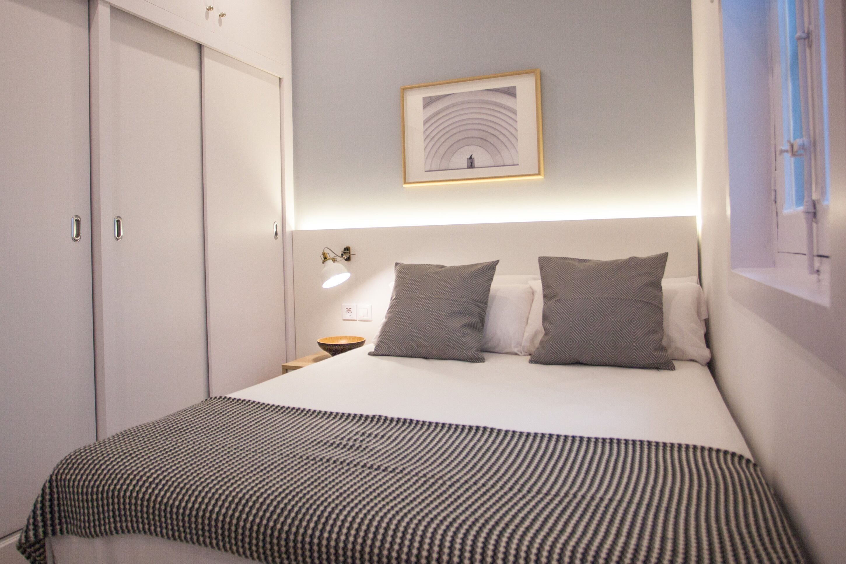 A bedroom with a bed, pillows, a bedside table, a lamp, and a framed picture on the wall.