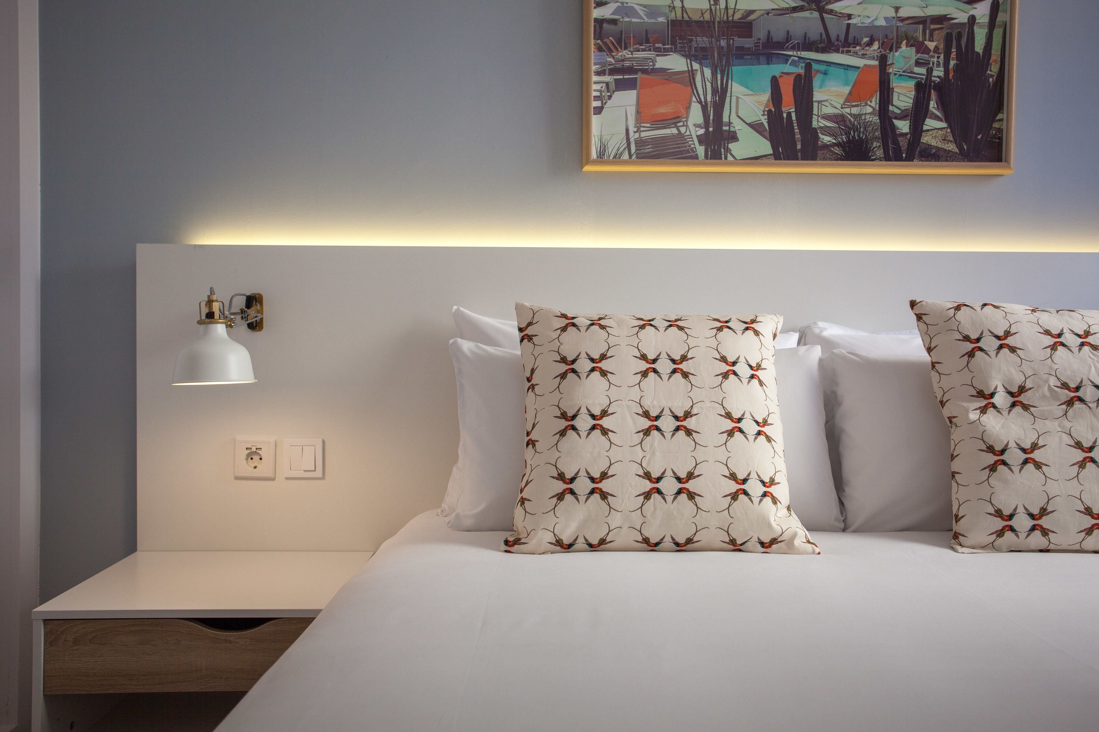 Una cama bien hecha con almohadas estampadas, una lámpara de noche y una lámpara de pared.