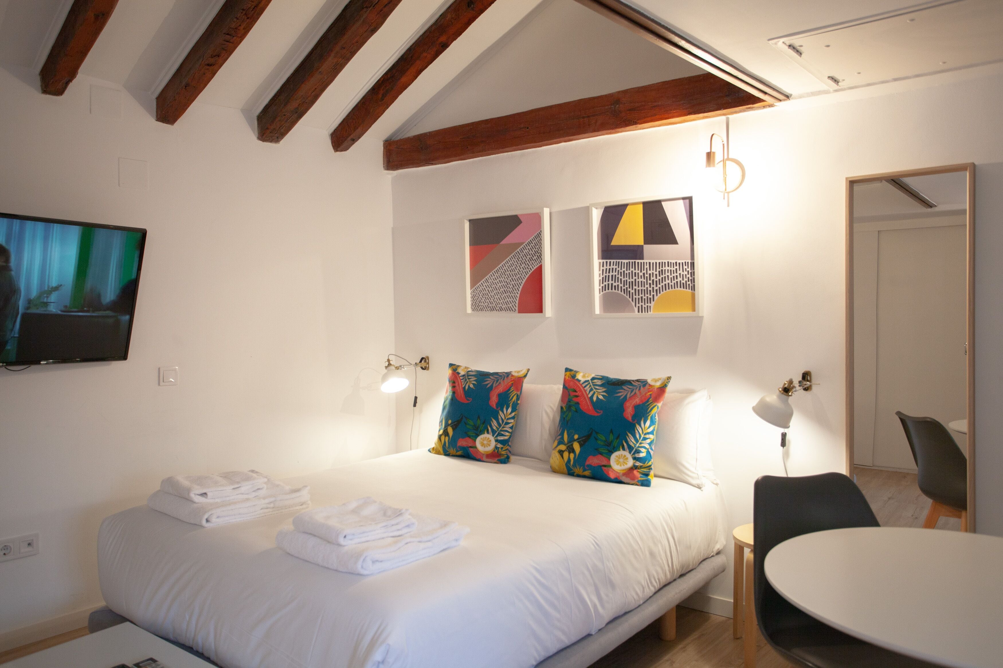 A hotel room with a bed, two pillows, a bedside table, a chair, and artwork on the wall.