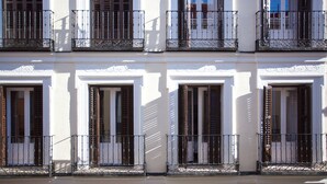 A multi-story building with white facades, multiple balconies with wrought iron railings, and windows with wooden shutters. - Gran Central Suites (Madrid)
