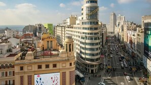 A cityscape with a prominent curved building featuring a Vodafone logo, surrounded by other buildings and a busy street. - Gran Central Suites (Madrid)