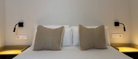 Een opgemaakt bed met twee kussens, twee nachtkastjes en twee wandlampen.