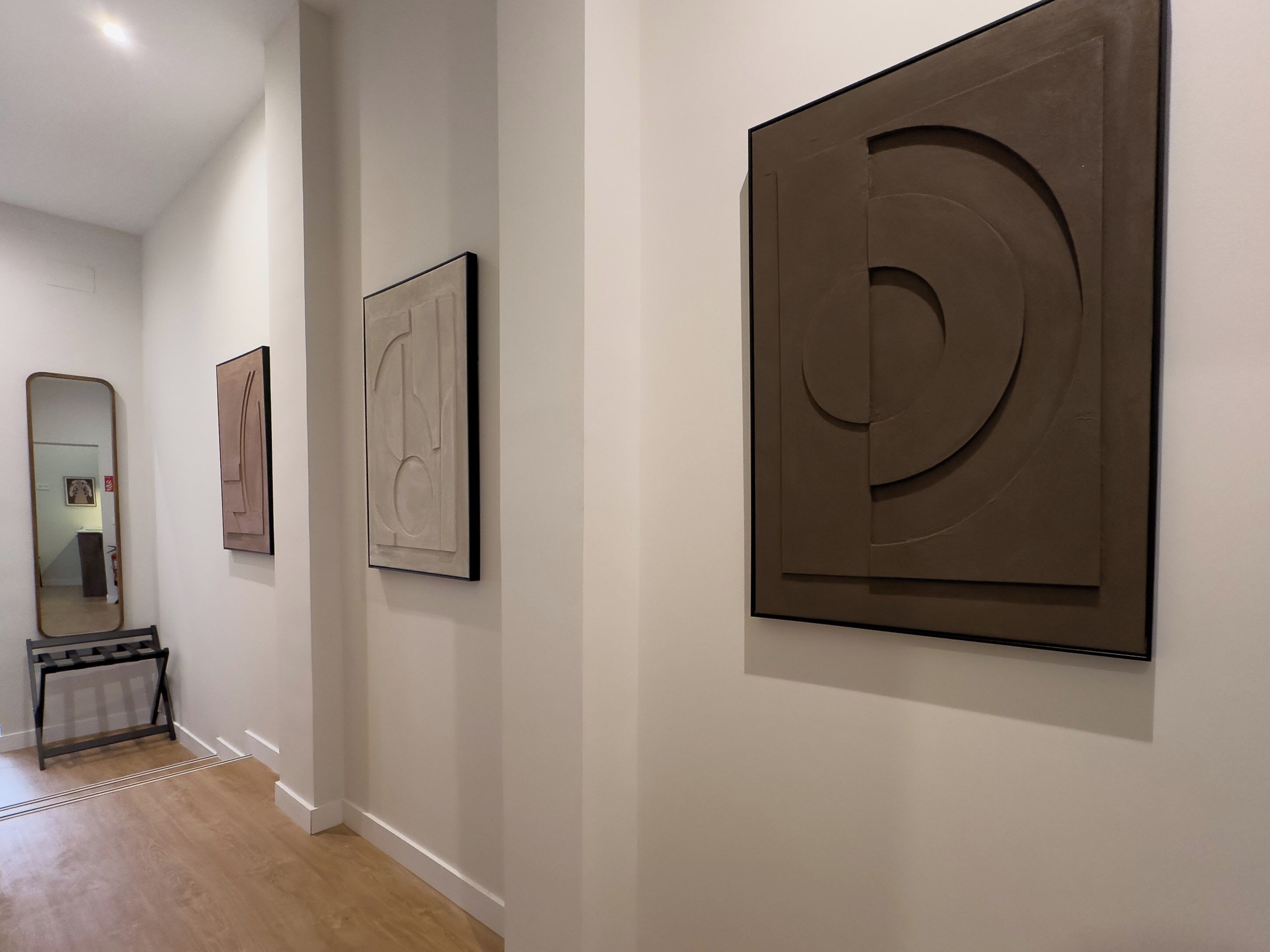 Ein Korridor mit drei abstrakten Kunstwerken an der Wand, einem Spiegel und einem Holzboden.