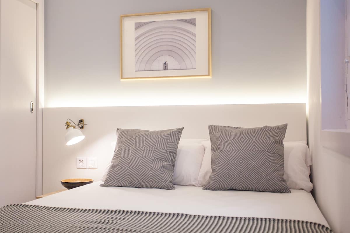 A neatly made bed with patterned pillows, a framed picture above it, and a bedside lamp.