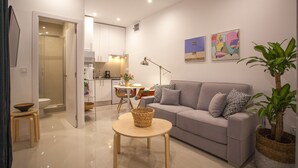 A modern living room with a grey sofa, a round wooden table, and a potted plant. - Gran Central Suites (Madrid)