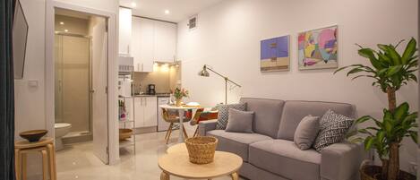 A modern living room with a grey sofa, a round wooden coffee table, and a dining area with colorful chairs.