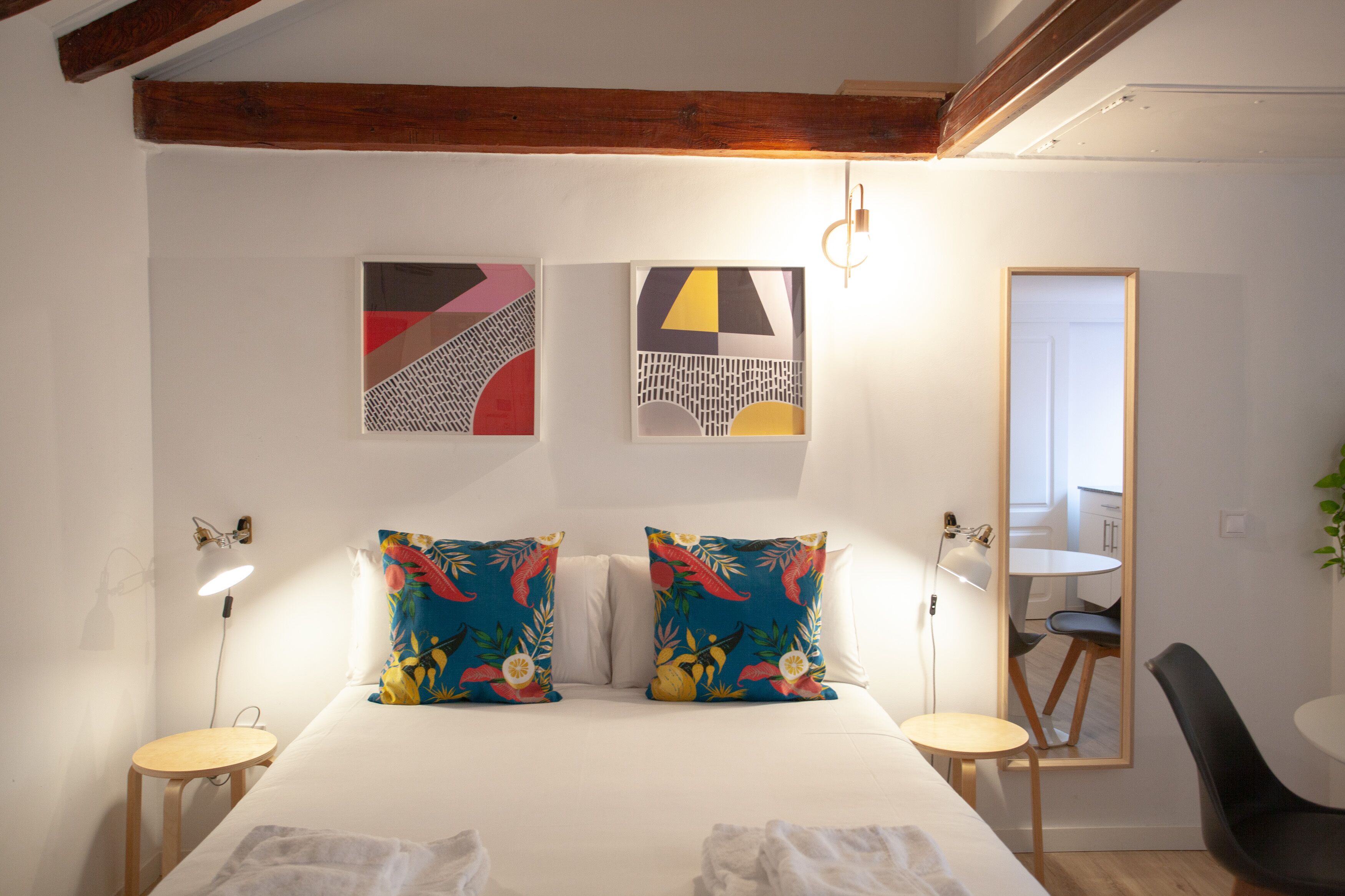 A bedroom with a bed, two bedside tables, a mirror, and artwork on the wall.
