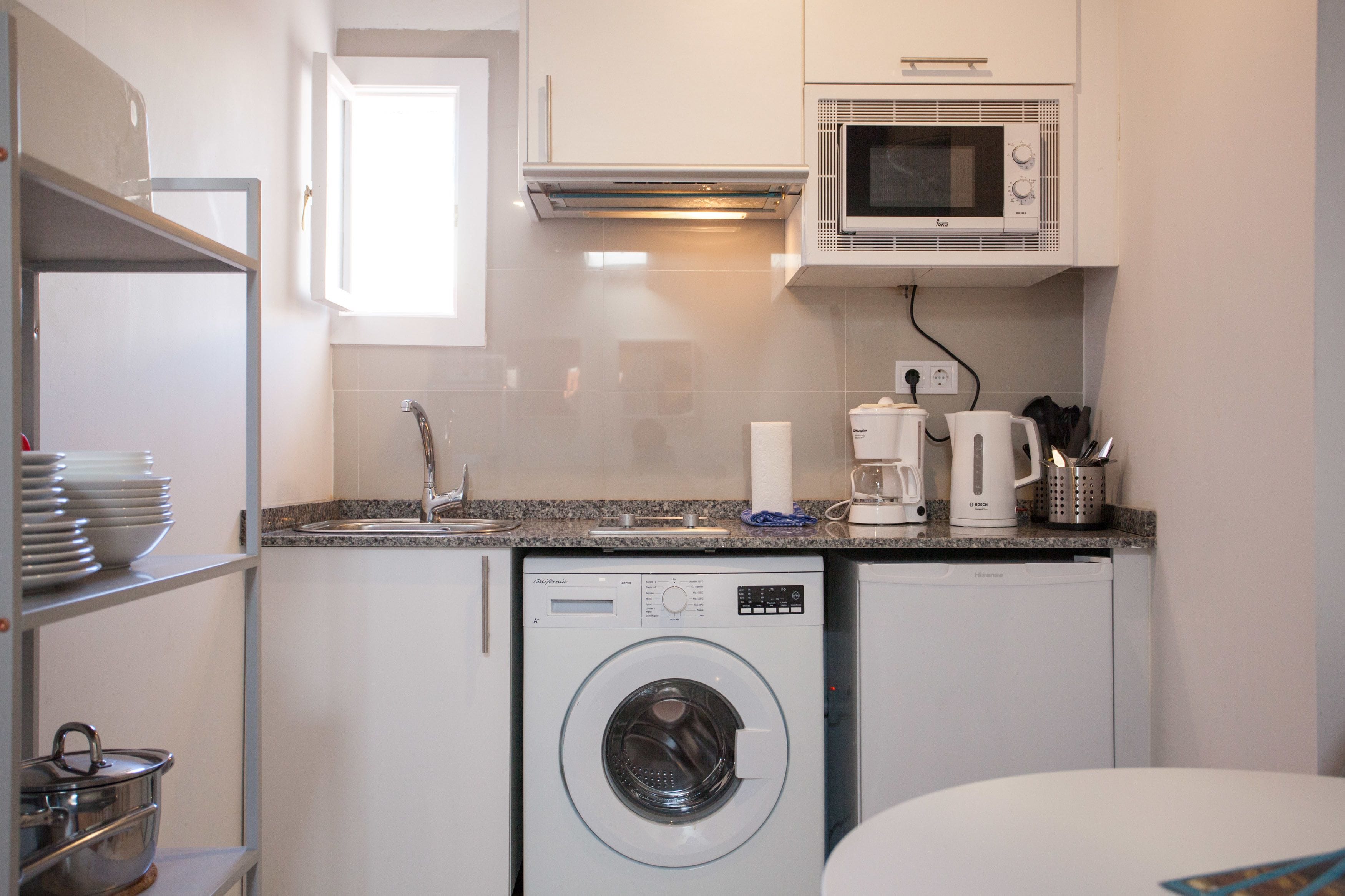 A compact kitchen with a washing machine, a microwave, and a coffee maker.