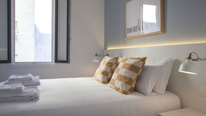 A neatly made bed with checkered pillows, a stack of white towels, and bedside lamps. - Gran Central Suites (Madrid)