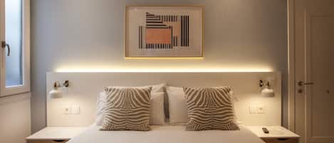 Un dormitorio con una cama grande, dos lámparas de noche, una obra de arte abstracta enmarcada y una puerta.