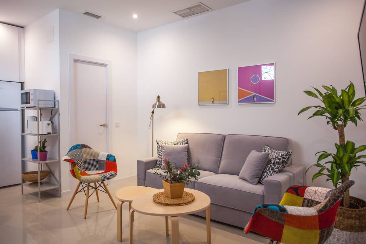 A modern living room with a grey sofa, colorful chairs, a small table, and a potted plant.