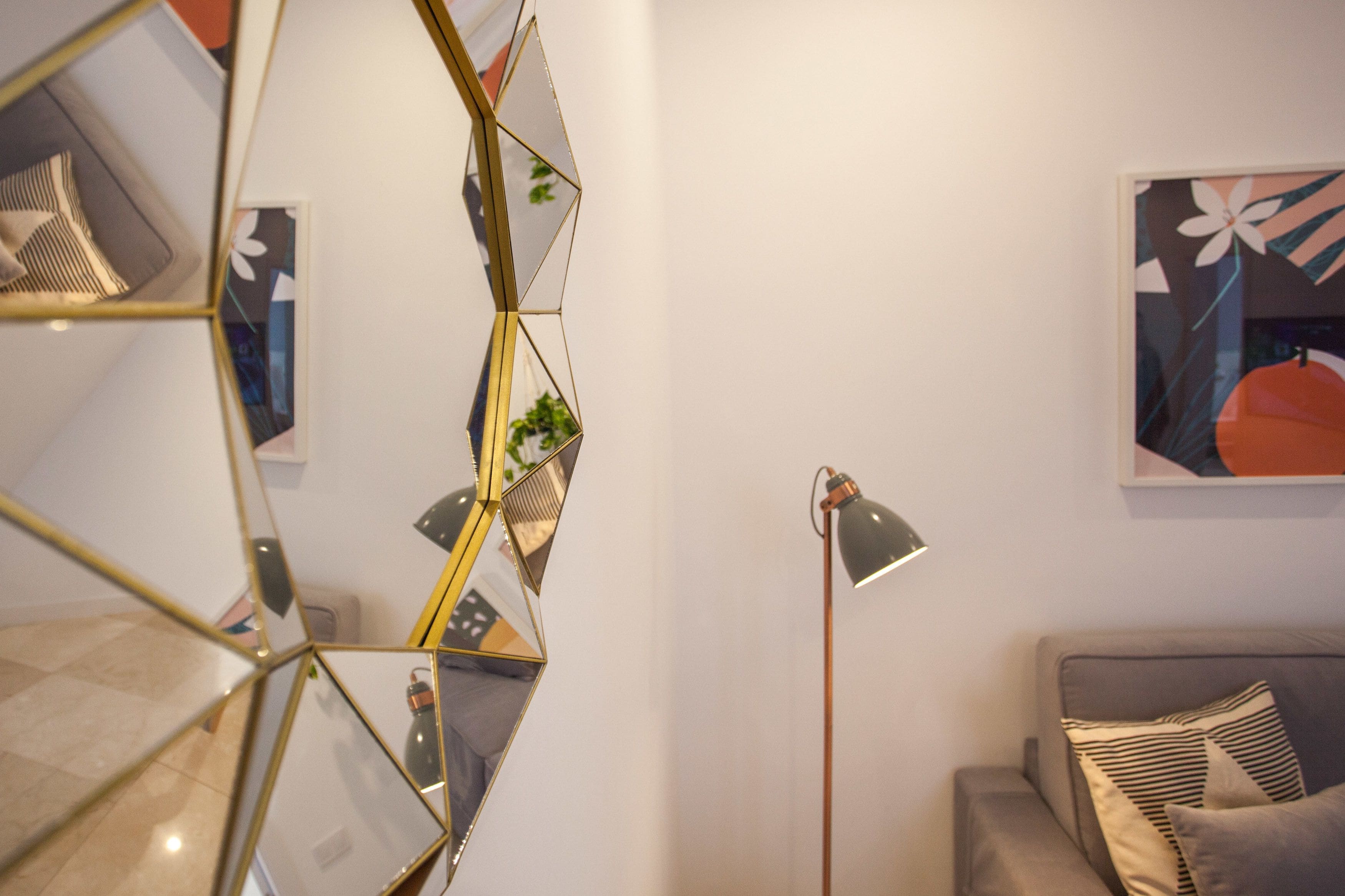A modern living room with a geometric mirror wall, a floor lamp, a sofa, and a framed artwork on the wall.