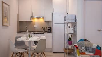 Een moderne keuken met witte kastjes, een inbouwoven en een koelkast. Er staat een eettafel met stoelen en een koffieapparaat.