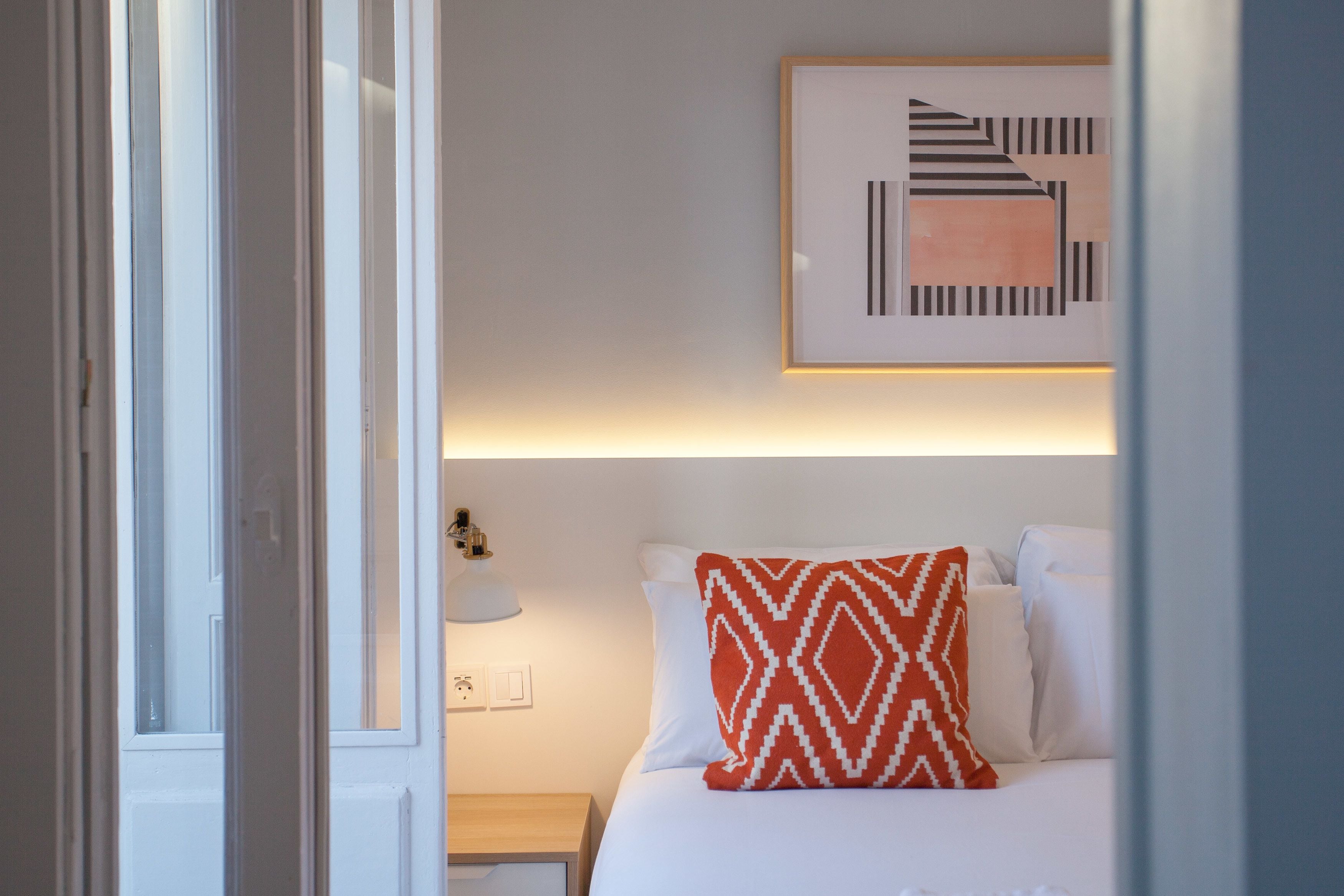 Una habitación de hotel con cama, mesita de noche, lámpara y una obra de arte colgada en la pared.