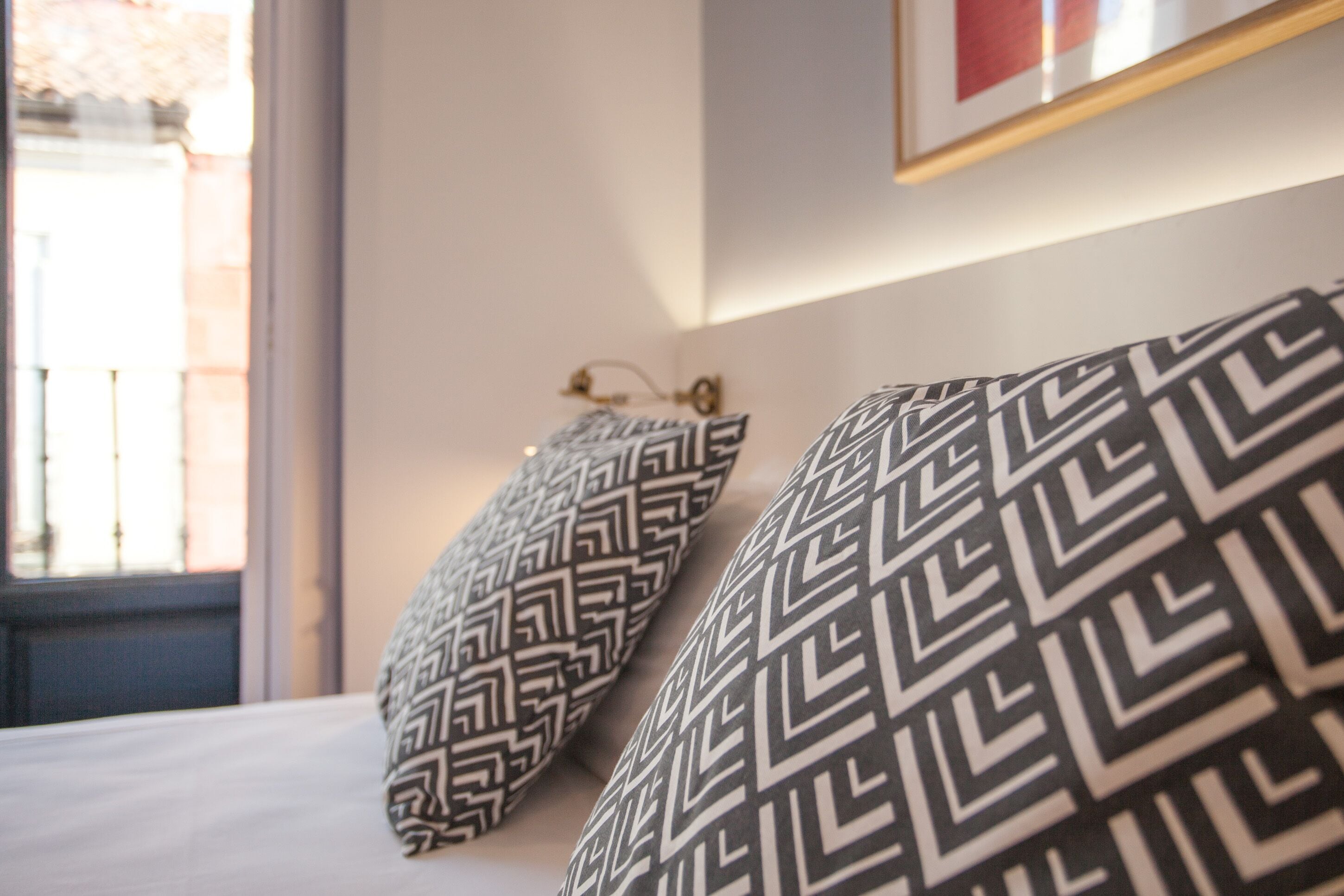 Een bed met gekleurde kussens en een lijst met een afbeelding aan de muur.