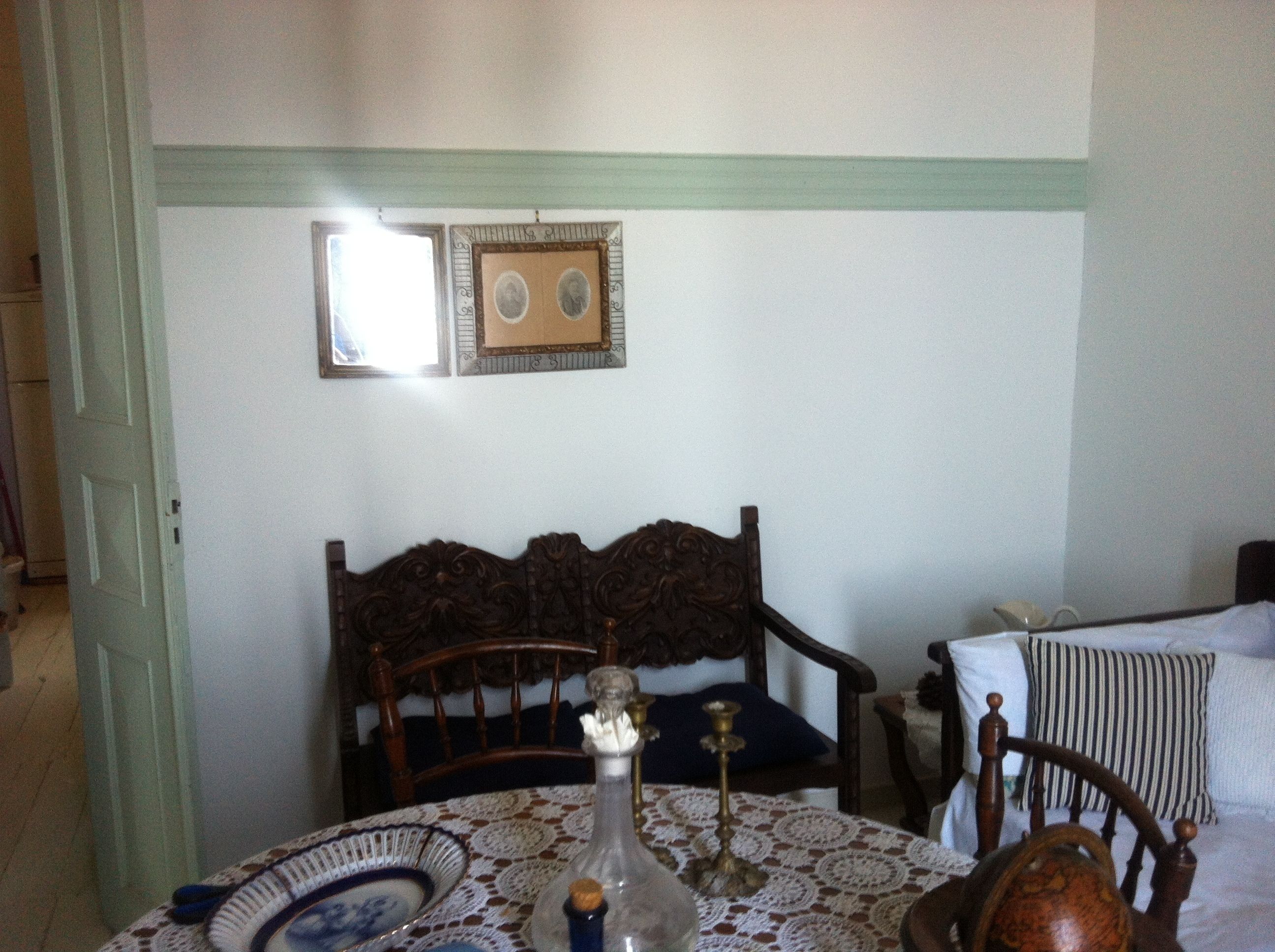 A dining area with a table set for two, a wooden chair, a lace tablecloth, and a wall-mounted picture frame.