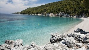 A coastal beach with clear turquoise water, rocky shoreline, and a forested hillside. - Persefonis view house (Skopelos)