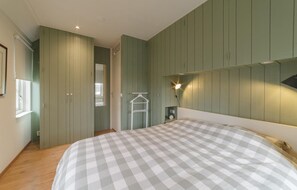 Een slaapkamer met een bed, een kledingkast, een spiegel, een hangrek en een wandlamp.