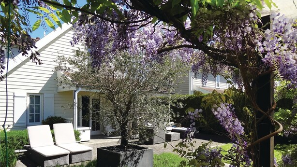 Ett hus med en veranda, utomhusmöbler och lila blommande klätterväxter.