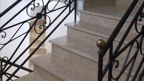 Una escalera con barandillas de metal negro ornamentadas y peldaños de mármol color beige.
