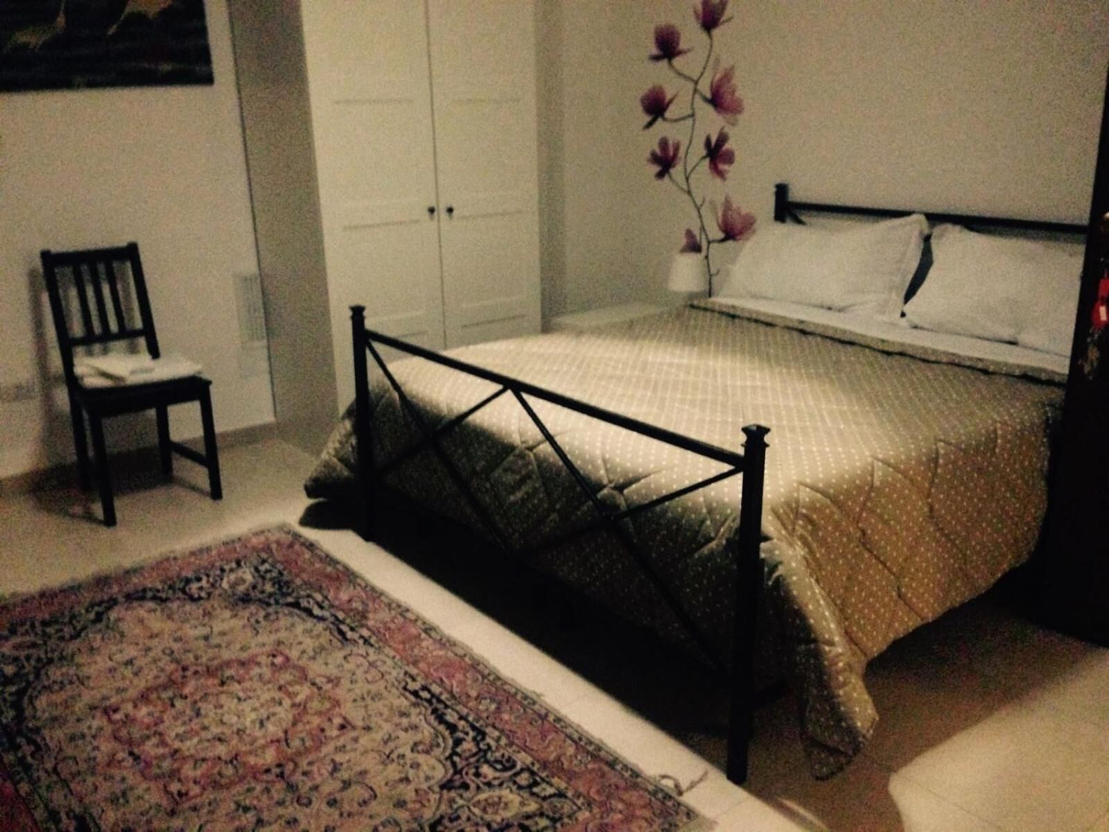 A bedroom with a bed, a chair, a wardrobe, and a floral wall decoration.