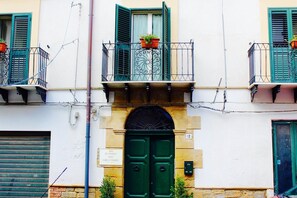 A building with a green door, a balcony with potted plants, and a sign above the door. - B&B Largo Barile (Caltanissetta)