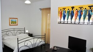 Un dormitorio con cama, televisor, un cuadro y una ventana con cortinas.
