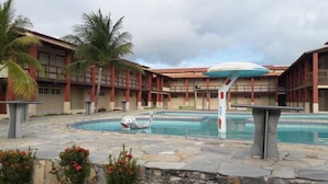 A swimming pool with a dolphin sculpture, palm trees, and a building with a red roof. - Porto Praia Hotel (Barra dos Coqueiros)