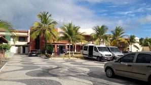 A parking area with several vehicles, palm trees, and a building with a red roof. - Porto Praia Hotel (Barra dos Coqueiros)