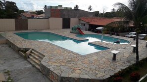 A swimming pool with a stone deck, a slide, and a small island with a water feature.