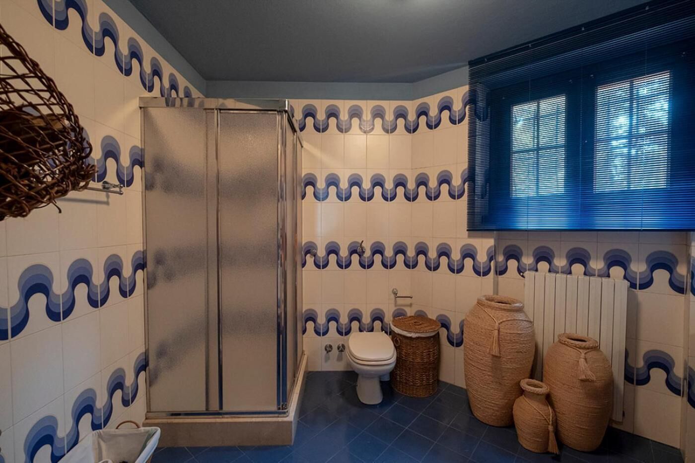 Casa de banho com chuveiro, sanita e grandes cestos de fibra natural.