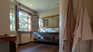 Un baño con un espejo grande, una ventana con rejas de metal, suelo de madera y un perchero.