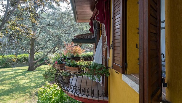 Un edificio amarillo con un balcón de madera, rodeado de vegetación y árboles.