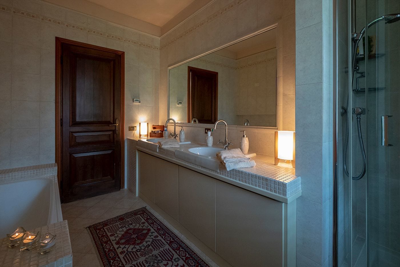 Ein modernes Badezimmer mit großem Spiegel, zwei Waschbecken, einer Dusche und einem dekorativen Teppich.