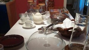 Una mesa de comedor dispuesta con vajilla blanca, incluyendo platos, tazas y una tetera, con una campana de cristal como centro y velas.