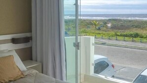 A hotel room with a large bed, a view of the ocean, and a balcony with a car parked outside. - Hotel Porto Fino (Pontal do Parana)