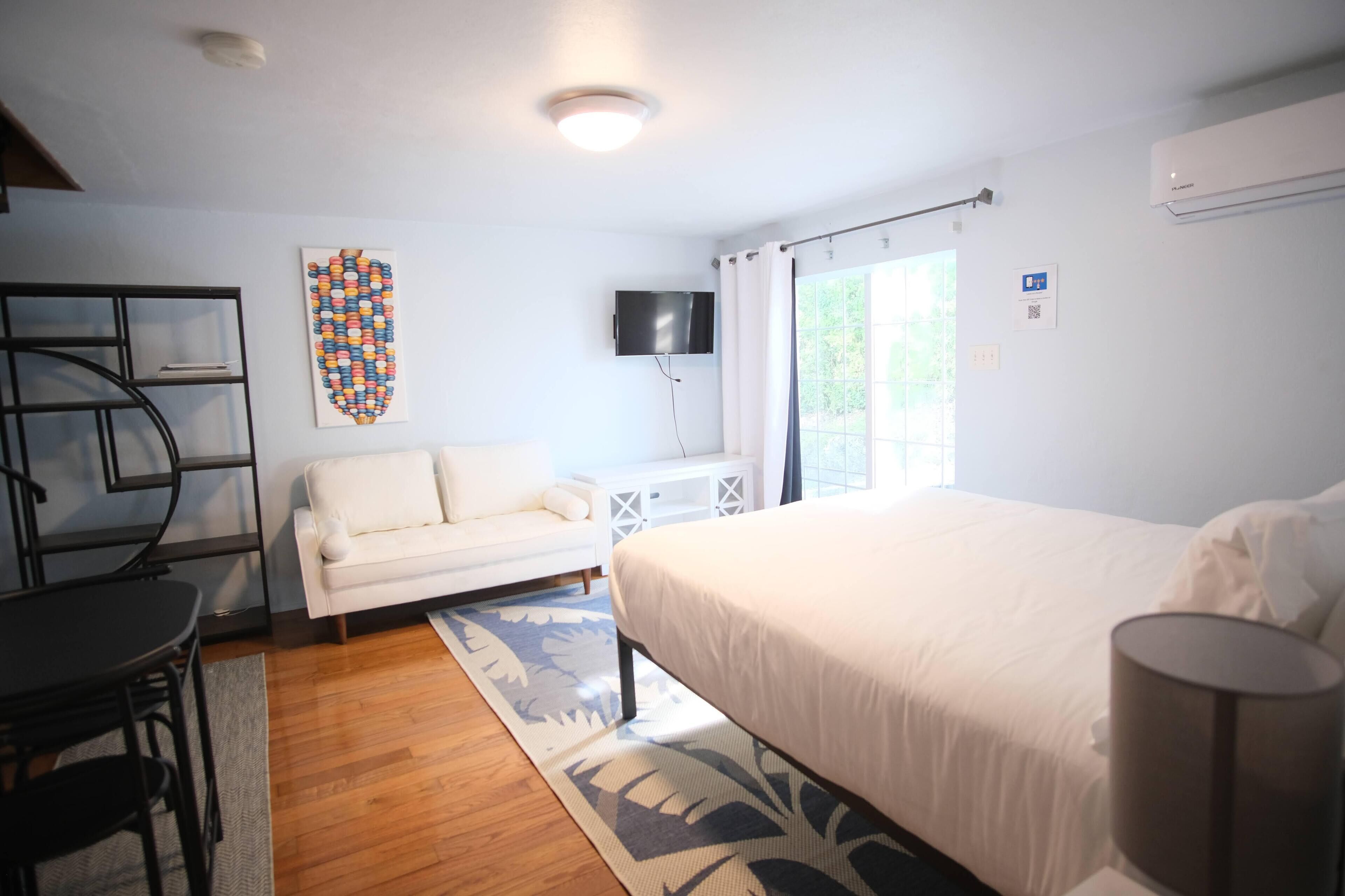 A bedroom with a bed, a white sofa, a TV, and a window with curtains.