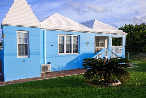 A two-story blue house with white trim, a covered porch, and a small garden with a palm tree.