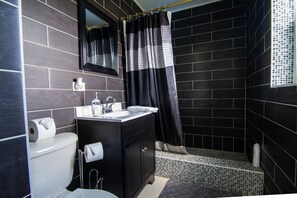 A modern bathroom with a black tiled shower, a white sink, and a toilet.