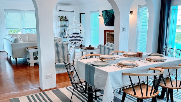 Un espace repas avec une longue table dressée pour six personnes, entourée de chaises, dans une pièce aux murs blancs et au plancher en bois.