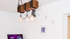 Un coin repas avec une table en bois, quatre chaises marron, un luminaire suspendu, un téléviseur à écran plat et une horloge murale.